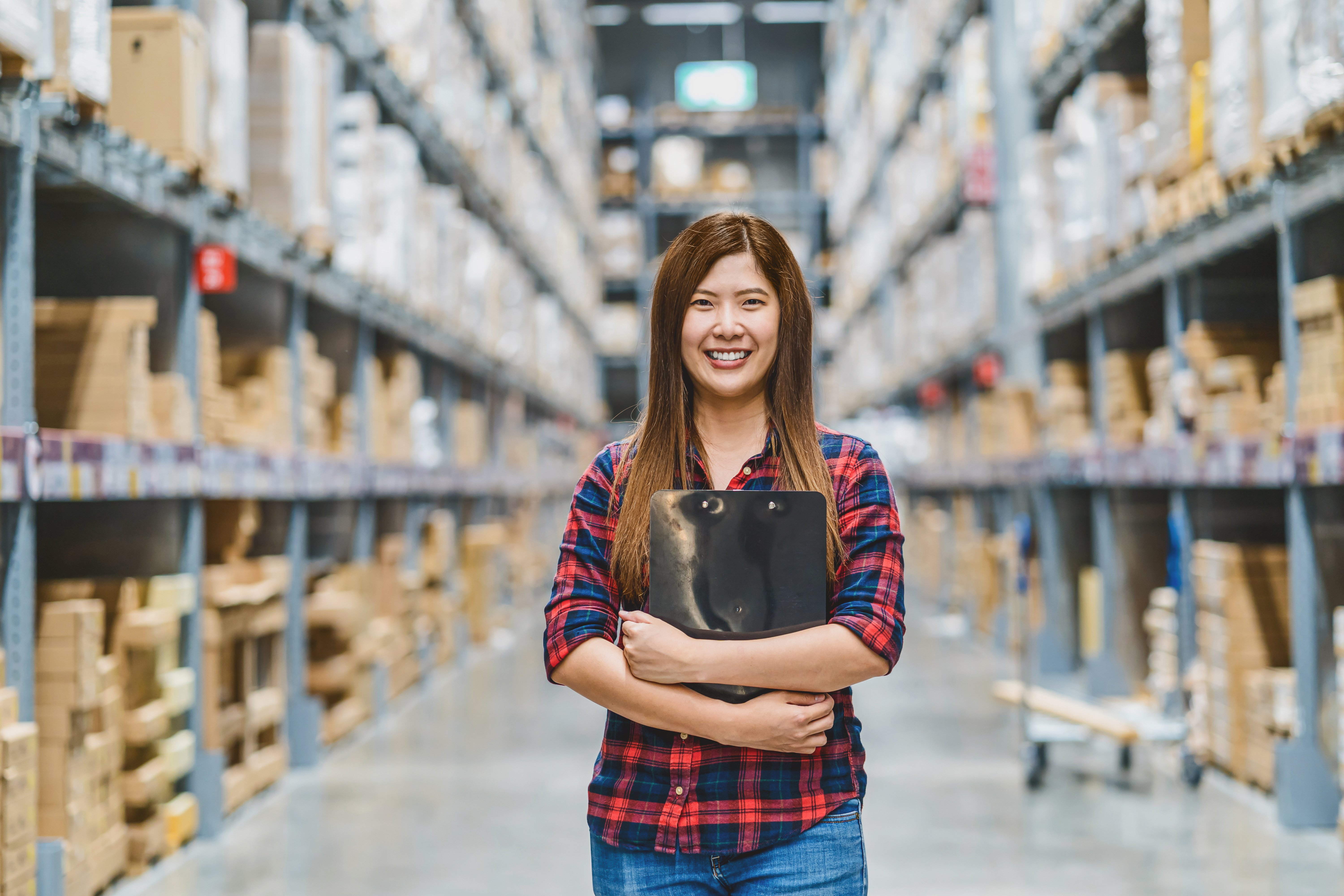 Smiling professional standing in a warehouse, representing strategies for B2B manufacturing marketing success through organized inventory management and effective marketing approaches.