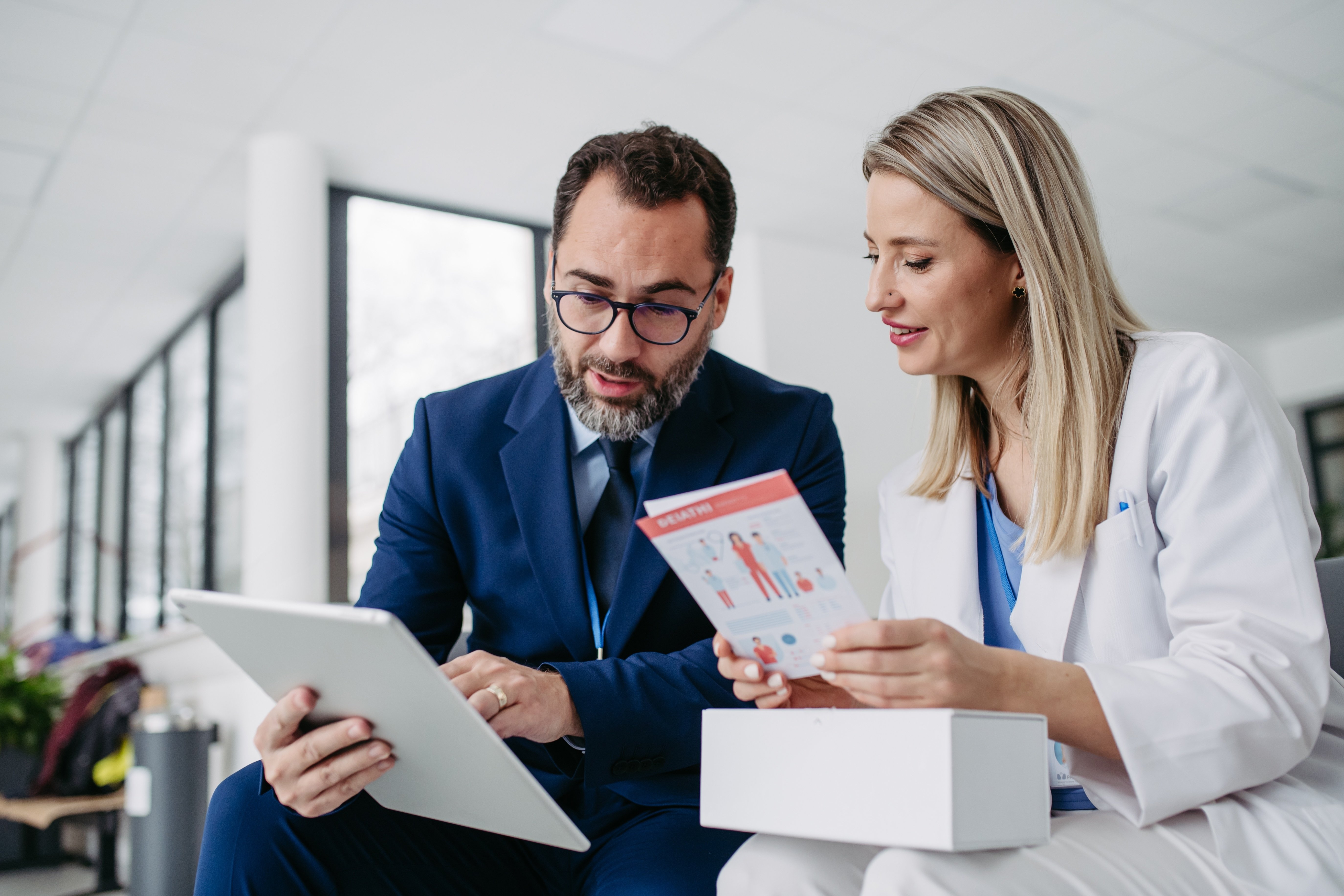 Two professionals reviewing healthcare marketing materials, including a digital tablet and printed patient-focused content, illustrating effective cross-channel healthcare marketing solutions.