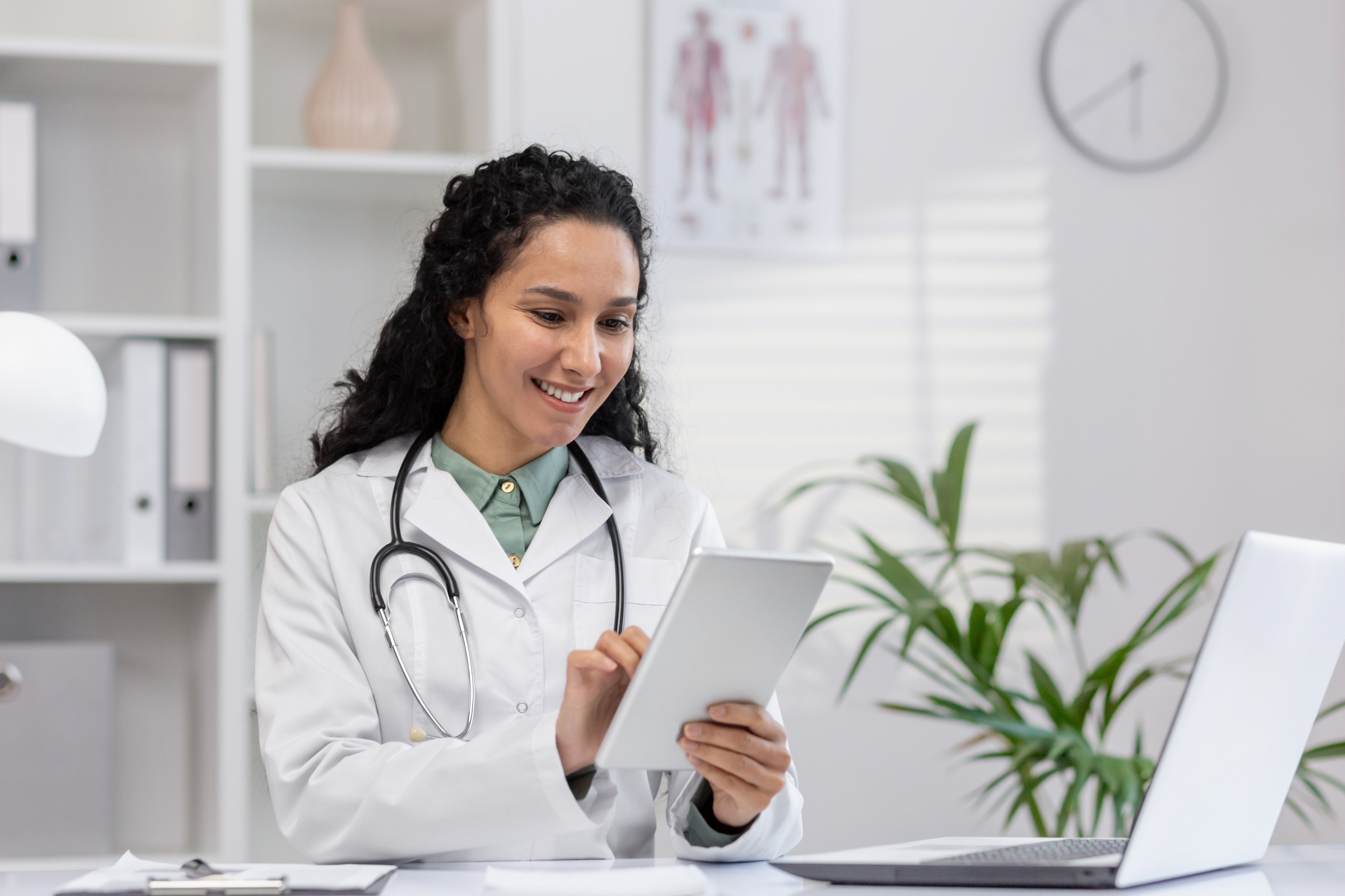 Smiling healthcare professional reviewing patient data on a tablet in a modern office setting, showcasing the importance of marketing in the healthcare industry to enhance patient engagement and streamline communication.